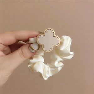 Detailed macro view of cream satin clover scrunchie held in hand with smooth texture