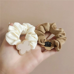 Detail of satin scrunchies with clover charm and hand made label in neutral tones