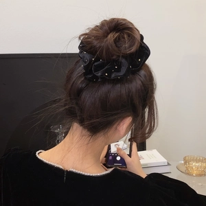 Chouchou élégant en velours noir clouté d'or sur un chignon de femme dans un décor cosy