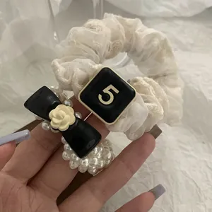 Close-up of pearl bead hair tie with black bow and cream camellia floral charm detail
