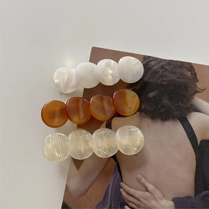 Detail of three acetate hair clips in pearl white, amber brown, and beige textures