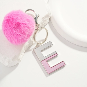 Pink plush pom-pom keychain with silver metal letter E pendant on white geometric stand