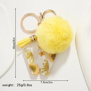 Detail view of yellow resin letter W keychain with floral inlay and soft plush pompom