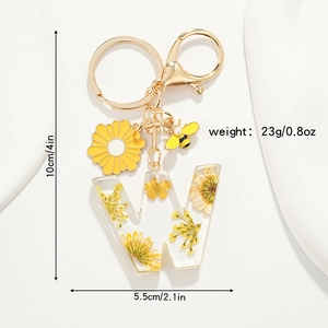 Détail du porte-clés en résine lettre W avec fleurs séchées jaunes et pendentif abeille