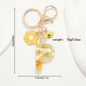 Détail du porte-clés en résine lettre P avec fleur séchée jaune et breloque abeille