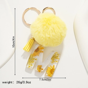 Detailed view of yellow faux fur pompom and resin letter M keychain with dried flowers