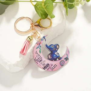 Detail of pink crescent moon keychain with blue elephant pattern and a gold tassel