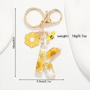 Détail du porte-clés lettre K en résine avec fleurs séchées jaunes et pendentif abeille