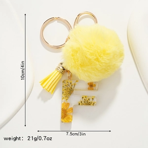 Detailed close-up of resin letter F keychain with yellow dried flowers and plush pompom