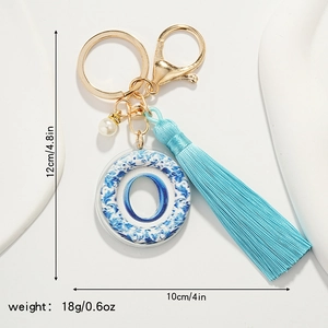 Blue porcelain letter O keychain with silk tassel and pearl detail on white background