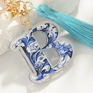 Blue porcelain style letter B keychain with silk tassel and pearl on white rock