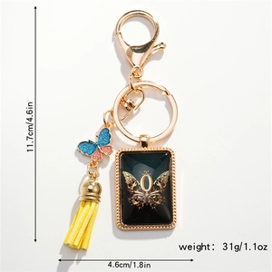 Detail of a butterfly keychain with yellow tassel and black rectangle charm with gold letter O