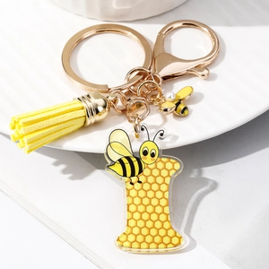 Detail of letter I acrylic keychain with honeycomb pattern, yellow tassel, and enamel bee