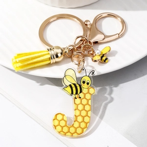 Macro detail of acrylic letter J keychain with yellow tassel and bee enamel charm