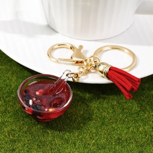 Macro detail of miniature food keychain bowl with red tassels and golden metal hardware