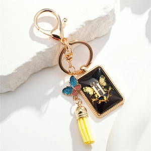 Golden butterfly letter H keychain with yellow tassel on white stone background