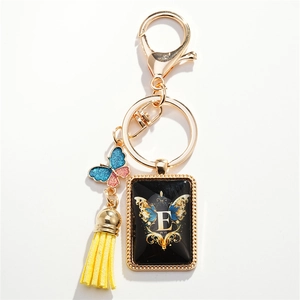 Golden butterfly keychain with letter E charm and yellow tassel on white background