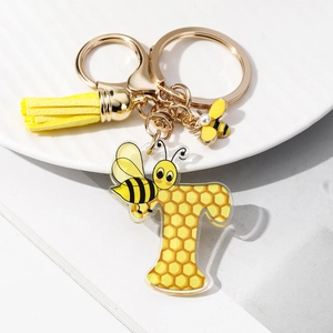Close-up of golden letter T keychain with yellow tassel and bee acrylic honey pattern