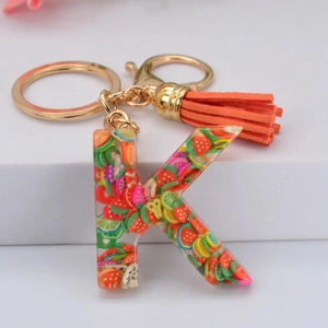 Détail porte-clés lettre K en résine avec tranches de fruits et pompon orange suède