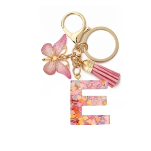 Close-up of resin letter E keychain with pink sequins, butterfly charm and tassel details