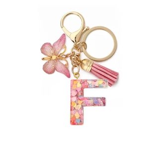 Detail of resin letter F keychain with pink sequins, butterfly charm and tassel fringe