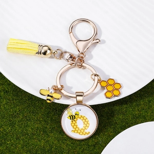 Macro detail of bee keychain featuring letter Q charm, yellow tassel, and golden metal honeycomb
