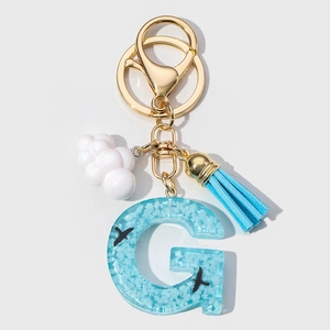 Blue resin letter G keychain with white clouds, flying birds, and blue suede tassel