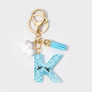Detail of blue resin letter K keychain with cloud patterns, tassel, and gold hardware