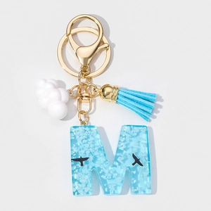 Detail of blue resin letter M keychain featuring white clouds and a blue silk tassel
