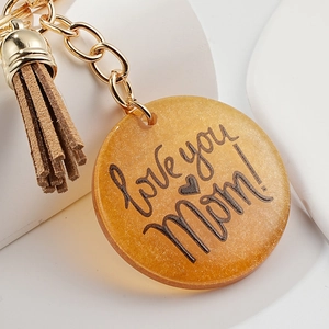 Détail macro du porte-clés Mom en résine pailletée avec pompon en daim marron chic