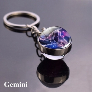 Macro shot of silver Gemini constellation glass ball keychain on reflective black surface