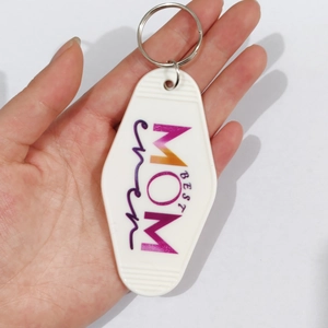 Close-up of hand holding a white vintage motel key tag with colorful Best Mom Ever text