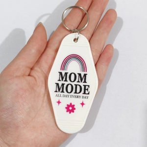 Close-up of white motel style keychain with MOM MODE print held by hand