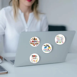 Detail view of four colorful 25mm glass fridge magnets showing cartoon designs on a laptop
