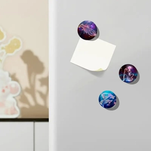 Detailed view of three zodiac glass fridge magnets holding a paper note on a white surface