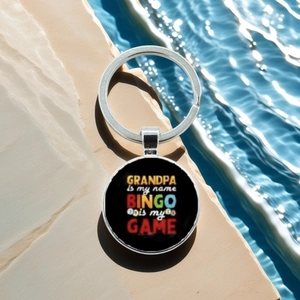Bingo keychain with Grandpa slogan displayed over clear blue water on rock edge