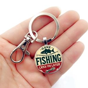 Détail d'un porte-clés de pêche argenté avec texte Gone Fishing tenu à la main sur fond clair