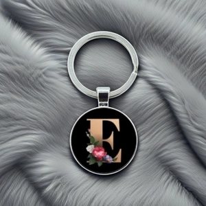 Close-up of metal keychain featuring letter E with floral pattern on grey plush background