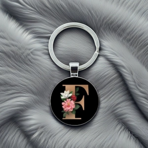 Detail of round metal keychain featuring an elegant golden letter F with floral accents