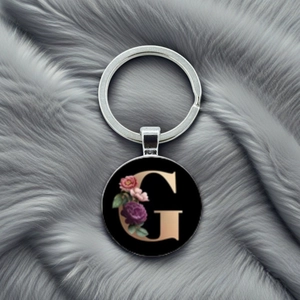 Detail of silver letter G keychain with floral patterns on polished black background