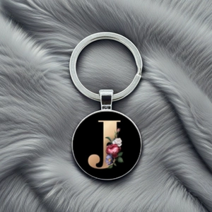 Macro shot of letter J keychain with floral pattern on a grey plush background