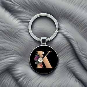 Detail of round keychain with golden letter K and elegant floral design on black background