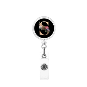 Detail of retractable badge holder with letter S and floral patterns on black background