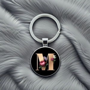 Detailed close-up of a round alphabet M keychain with floral patterns on grey faux fur