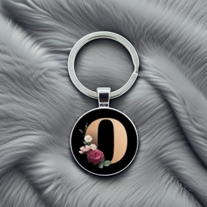 Close-up of alphabet letter O glass dome keychain with elegant floral pattern over grey fur