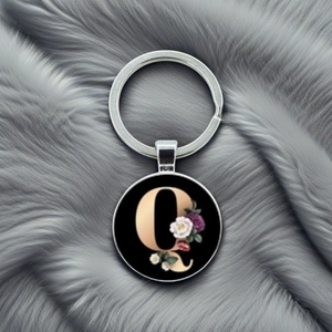 Close-up of circular metal keychain with golden letter Q and elegant floral art on gray fur