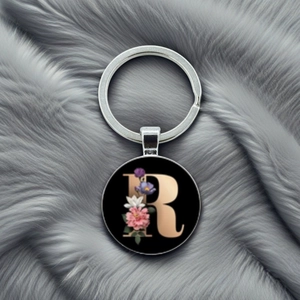 Detail of metal keychain with letter R and floral pattern on a grey plush surface