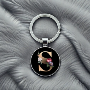 Close-up of a round silver keychain pendant featuring a gold letter S with floral design
