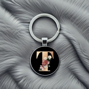 Detailed view of metal keychain featuring a black round pendant with floral letter T design