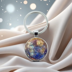 Detail showing space-themed art glass pendant keychain on beige silk fabric background